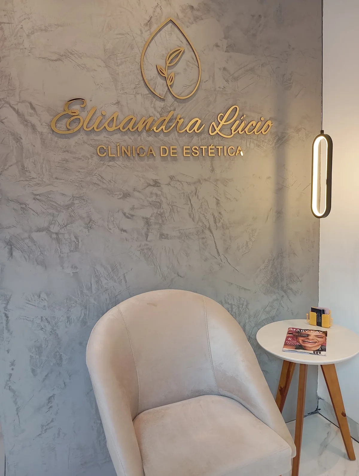 Recepção da clínica com poltrona e parede de mármore com logo dourada